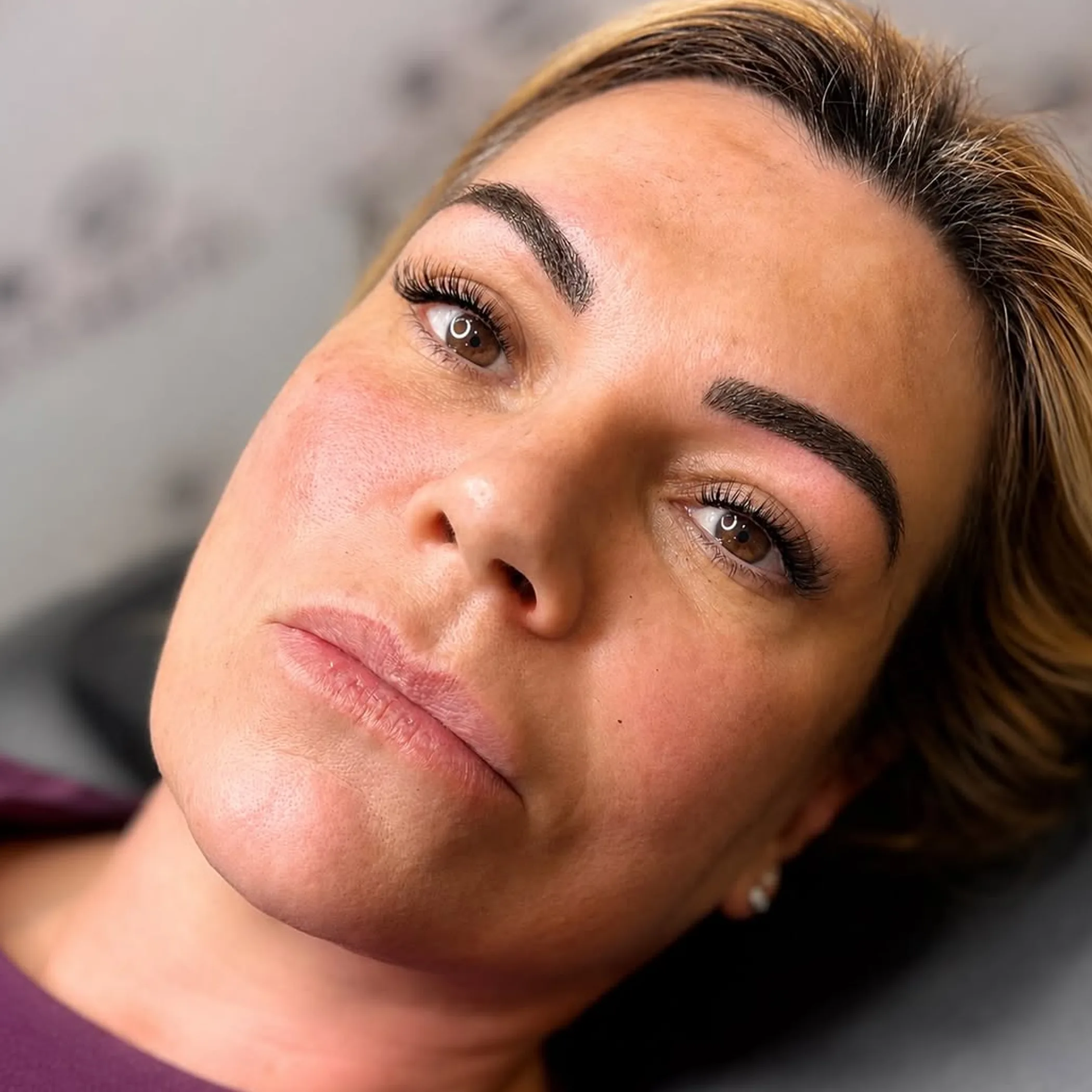 woman applying concealer to eyebrow tattoo